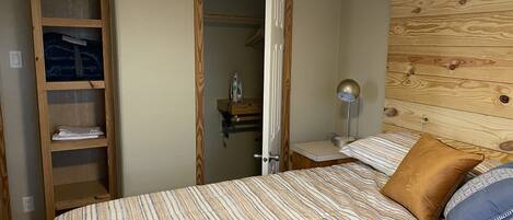 Een slaapkamer met een bed, een houten hoofdbord, een nachtkastje, een lamp en een kledingkast.