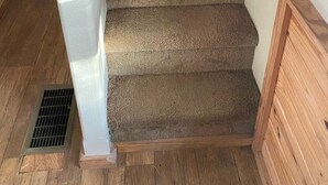 Una escalera alfombrada con barandillas de madera y una pared blanca.