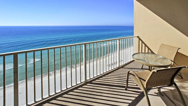 Ein Balkon mit Glastisch und Stühlen, der auf einen Strand und den Ozean blickt.