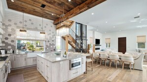 A modern kitchen with a central island, wooden ceiling beams, and a dining area with a sofa and chairs. - Coastal Dream|Short Walk to Beach Access|Private Pool|Gulf Views|Golf Cart (Santa Rosa Beach)