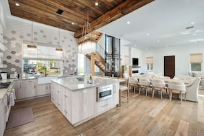 A modern kitchen with a central island, wooden ceiling beams, and a dining area with a sofa and chairs.