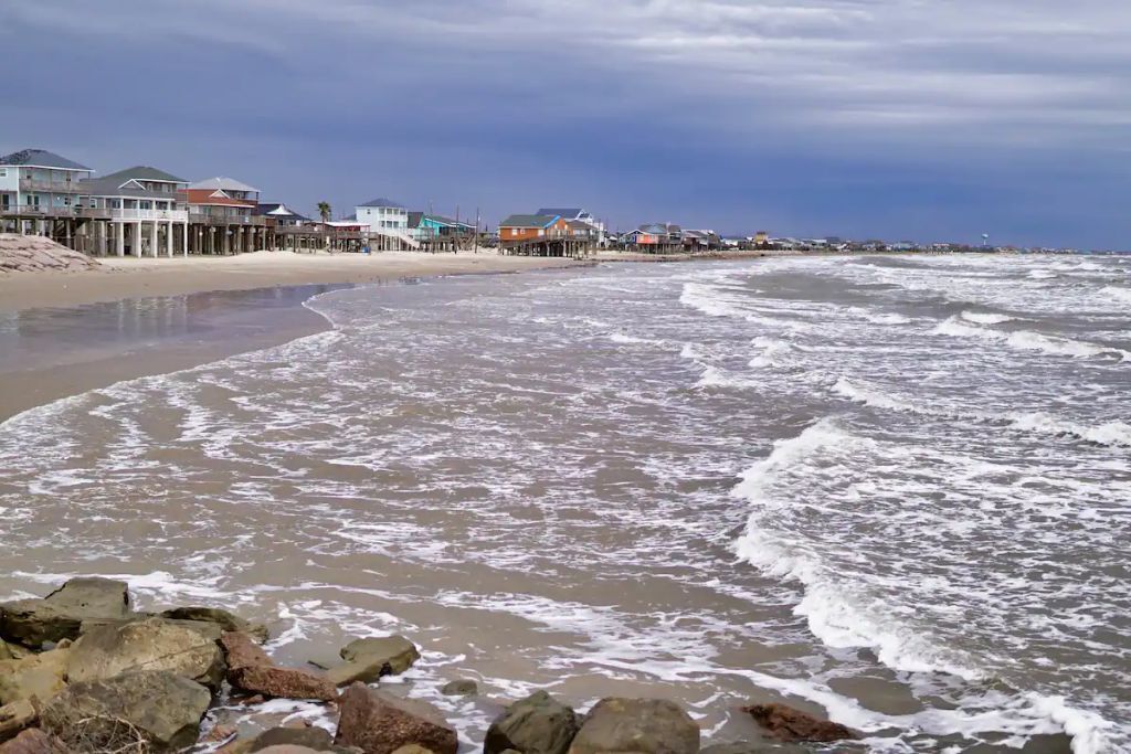A beach with waves and a row of houses along the shore.