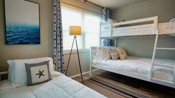 A hotel room with a bunk bed, a bed with a star-shaped pillow, a floor lamp, and a painting of the ocean.