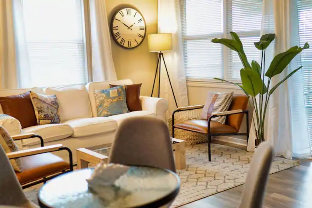 A living room with a sofa, armchairs, a coffee table, a floor lamp, and a large plant.