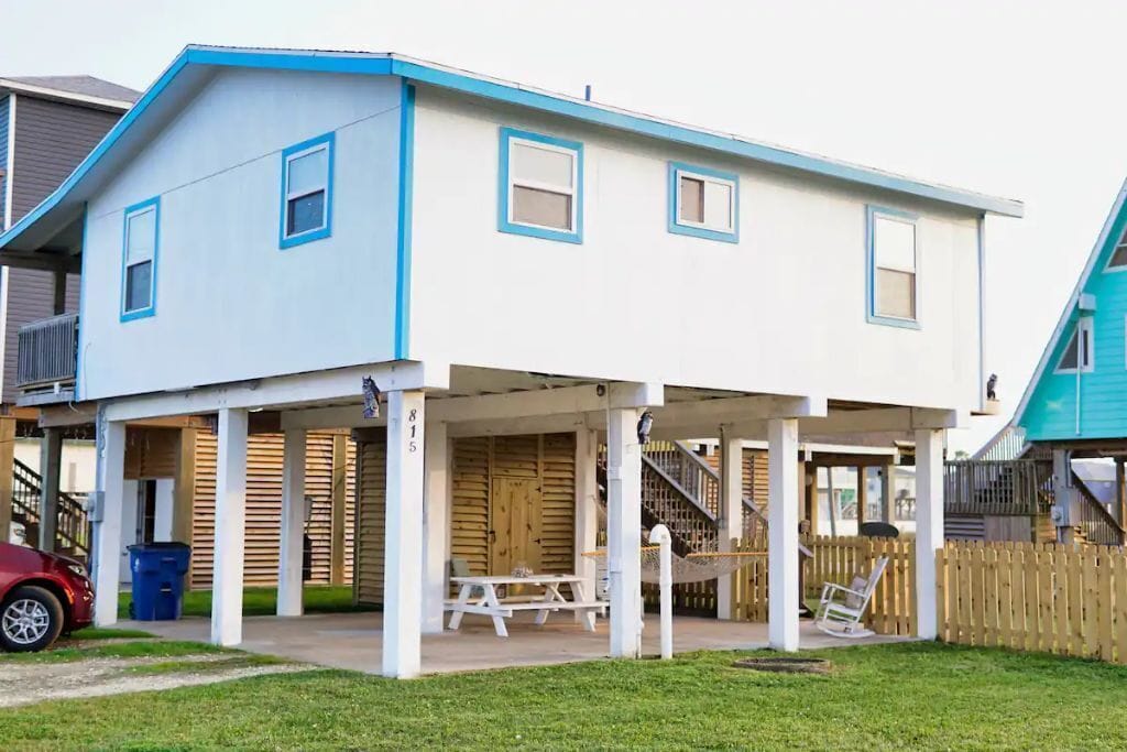 A two-story house with a covered porch, a picnic table, and a hammock.