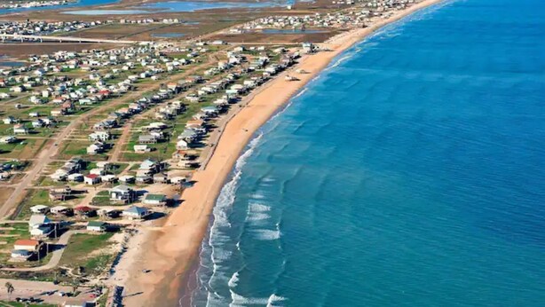 An aerial view of a coastal residential area with houses aligned along the beach, a sandy shoreline, and a clear blue ocean. - Serenity Sol ※ Surfside Charmer Near Beach & Jetty (Surfside Beach)