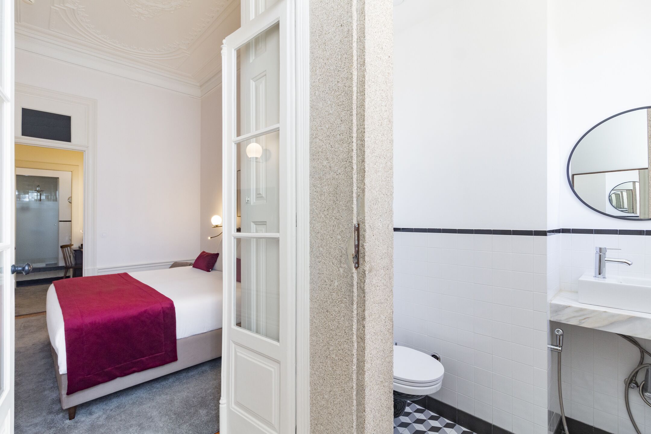 A hotel room with a bed, a bathroom with a toilet and sink, and a mirror.
