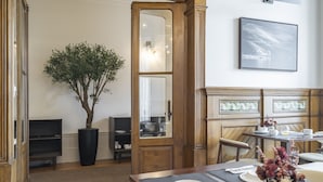 Un coin repas avec une table en bois dressée pour deux personnes, une plante en pot et un miroir.