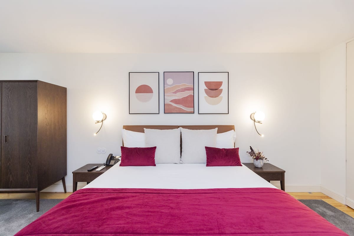 A neatly arranged bedroom with a large bed, a wardrobe, bedside tables with lamps, and wall-mounted artwork.