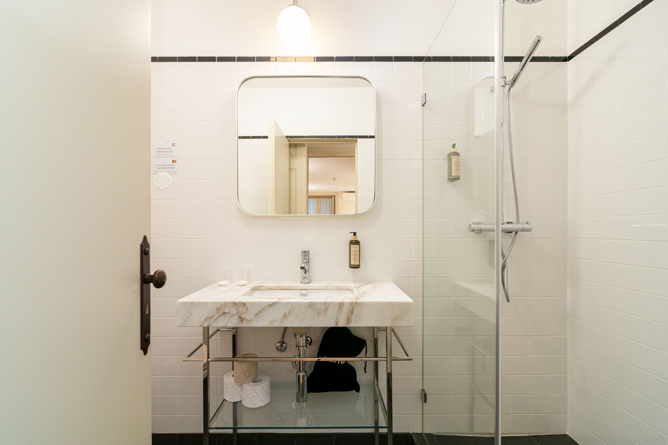 A bathroom with a white sink, a mirror, a glass shower enclosure, and a towel rack.