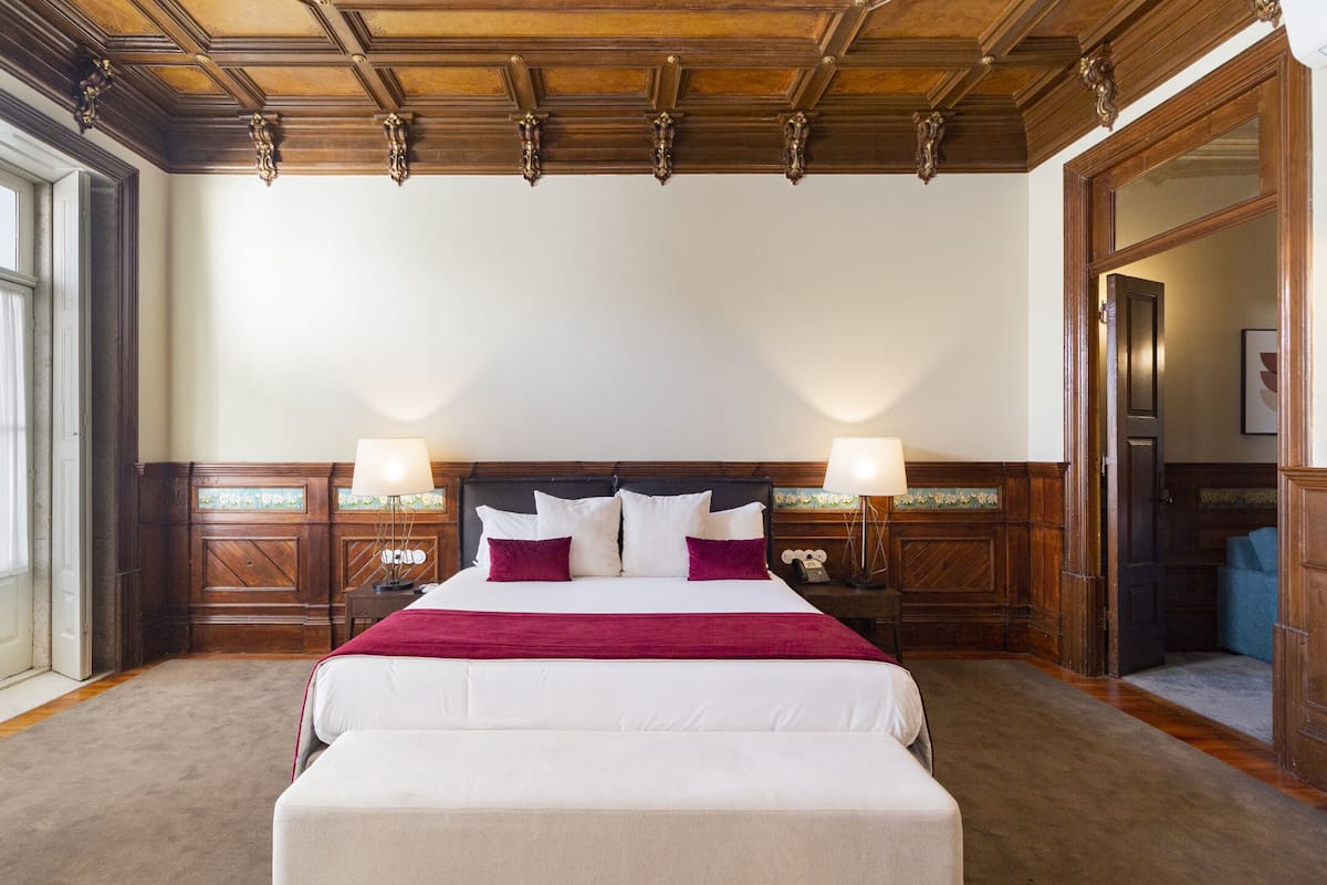 A hotel room with a large bed, wooden headboard, two bedside tables with lamps, and a large mirror.