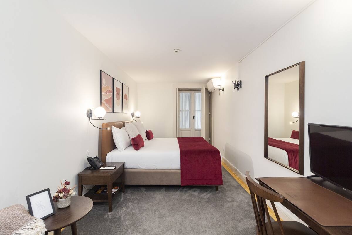 A hotel room with a bed, bedside table, lamp, chair, desk, and a TV.