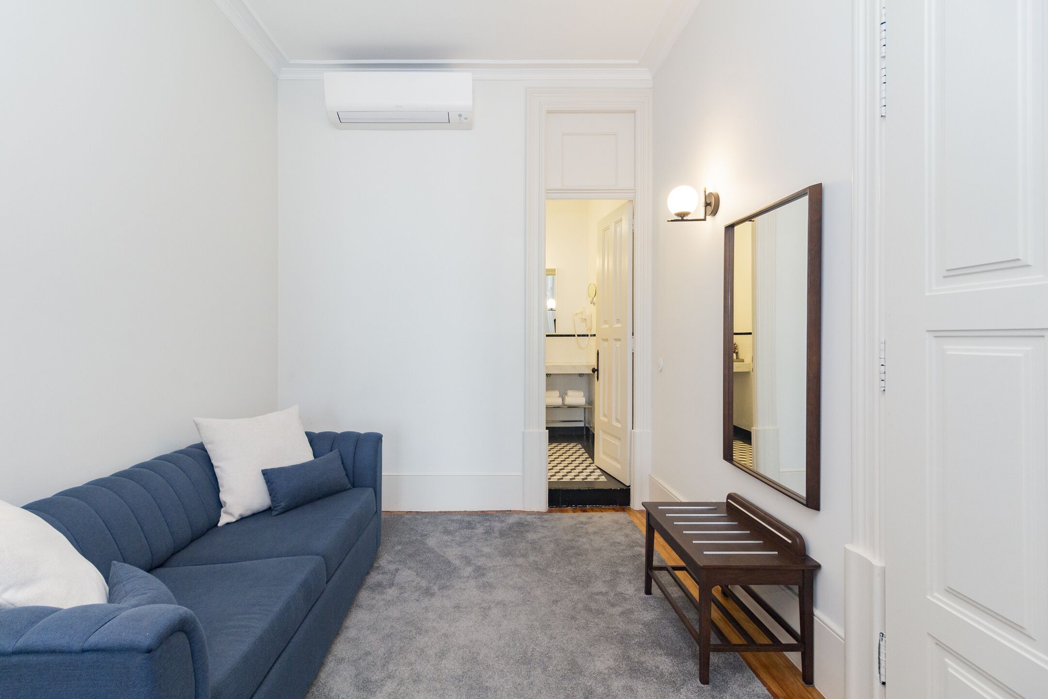 Un espace de vie compact avec un canapé bleu, un petit banc en bois et un grand miroir au mur.