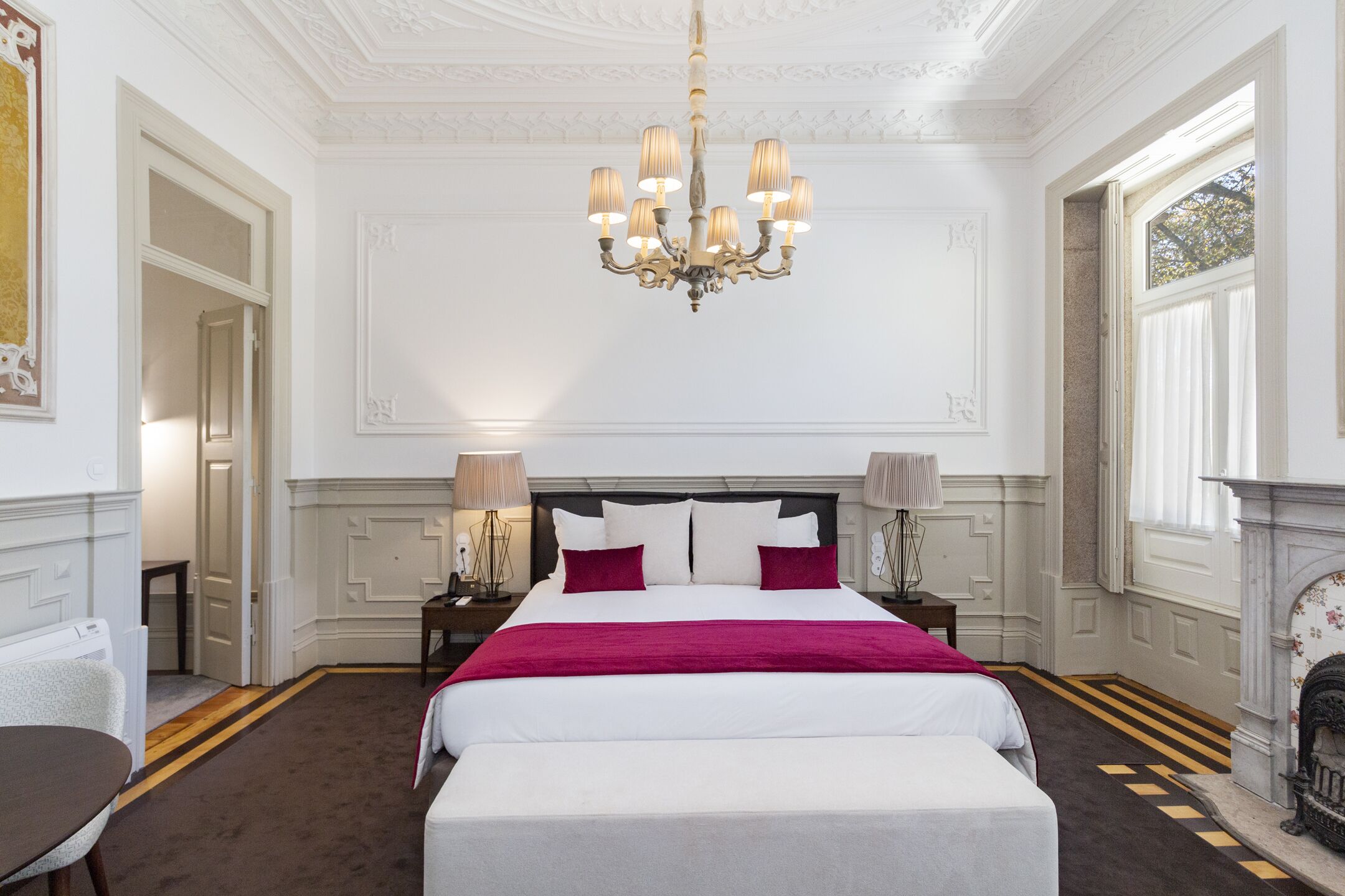 A spacious bedroom with a large bed, a chandelier, and a fireplace.