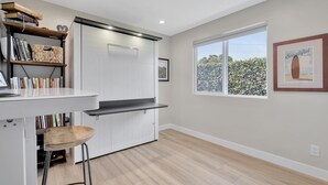Una cocina moderna con encimera blanca, taburete de madera y una estantería.