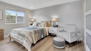 Un dormitorio con cama, mesitas de noche, una silla y una ventana.