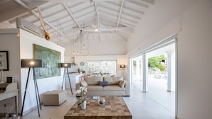 Un vaste espace de vie comprenant un grand salon avec une grande table basse en bois, un canapé et un coin repas agrémenté d’un mur de fond en pierre.