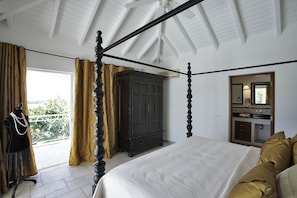 Une chambre à coucher avec un lit à baldaquin, une armoire en bois foncé, une coiffeuse avec un miroir et une vue sur la verdure par la fenêtre.