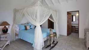 Une chambre avec un lit à baldaquin, un cheval à bascule, une table de chevet avec une lampe, et une vue sur la salle de bain par une porte ouverte.