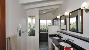 A modern bathroom with two sinks, a large mirror, and a view of greenery outside.