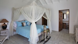 A bedroom with a canopy bed, a rocking horse, a bedside table with a lamp, and a view of the bathroom through an open door.