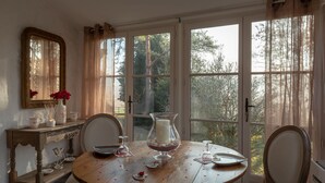 A dining area with a wooden table, chairs, a vase with flowers, and a window with a view of trees. - Romantic suite with private jacuzzi 1 hour from Paris (Vendières)
