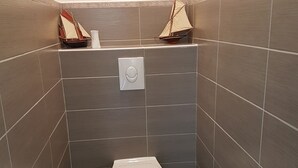 Um banheiro pequeno e moderno, com vaso sanitário, suporte de papel higiênico na parede e um modelo decorativo de navio.