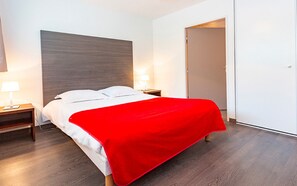 Ett hotellrum med en säng, ett nattduksbord, en lampa och en dörr.