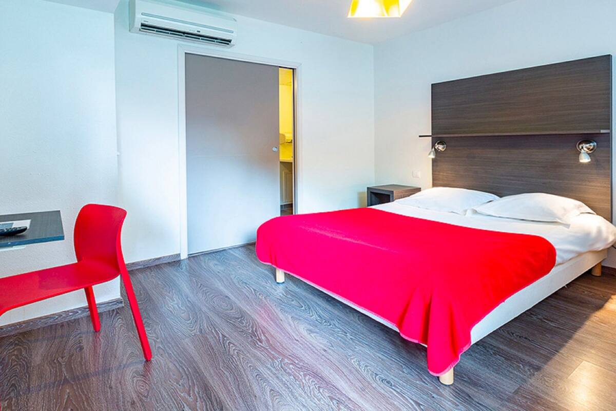 Ein modernes Hotelzimmer mit Bett, Schreibtisch, Stuhl und Kleiderschrank.