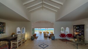 A spacious living area with a high ceiling, a dining table with chairs, a seating area with sofas, and a glass coffee table. - Oceane (2/4 Rooms) Luxury villa (Marigot)