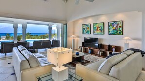 A spacious living room with a large sofa, a coffee table, a TV, and artwork on the wall. - Oceane (2/4 Rooms) Luxury villa (Marigot)
