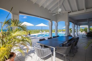 Un'area esterna coperta con piscina, tavolo da pranzo, sedie e ombrelloni.