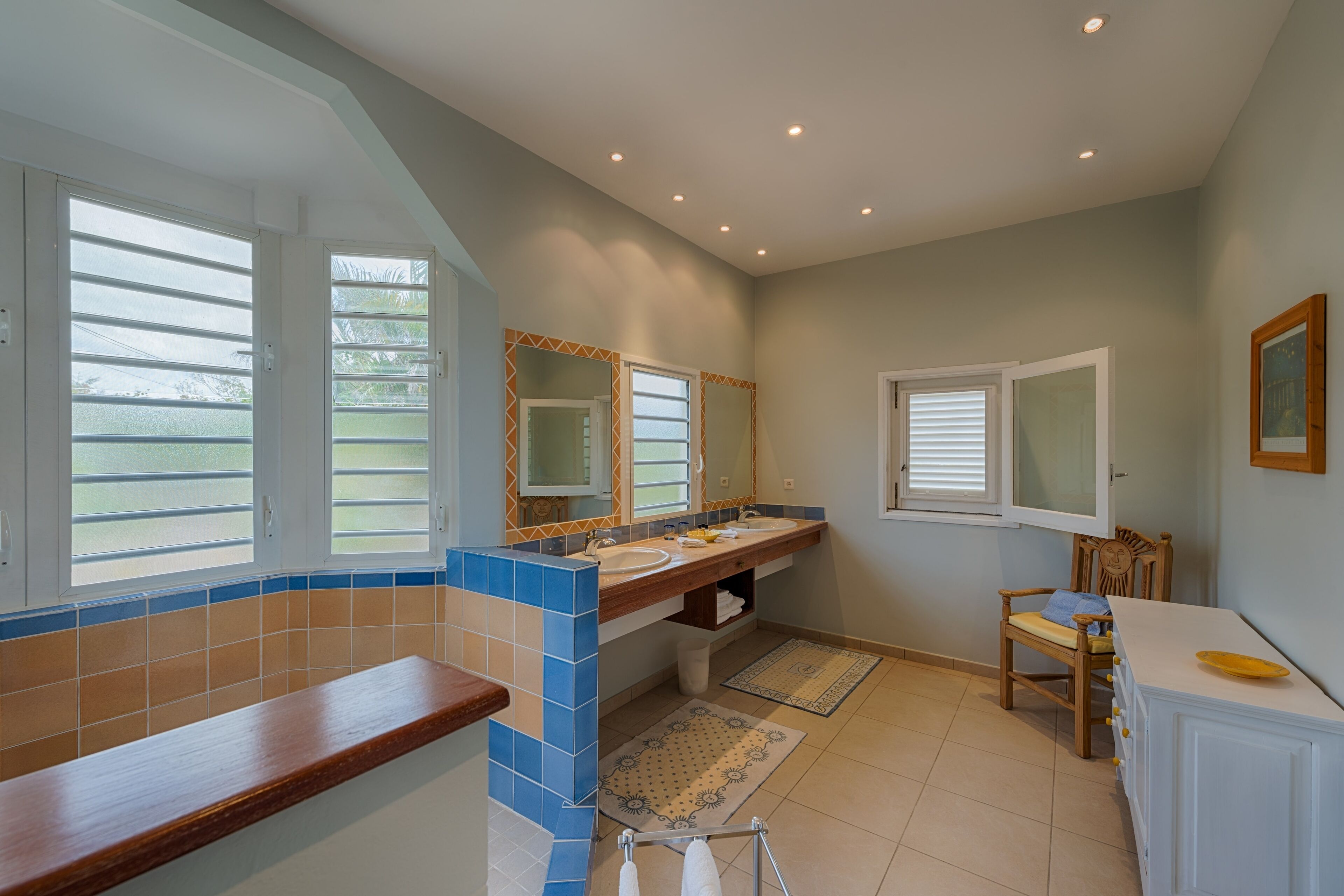A bathroom with a wooden vanity, two sinks, a large mirror, and a window with blinds.