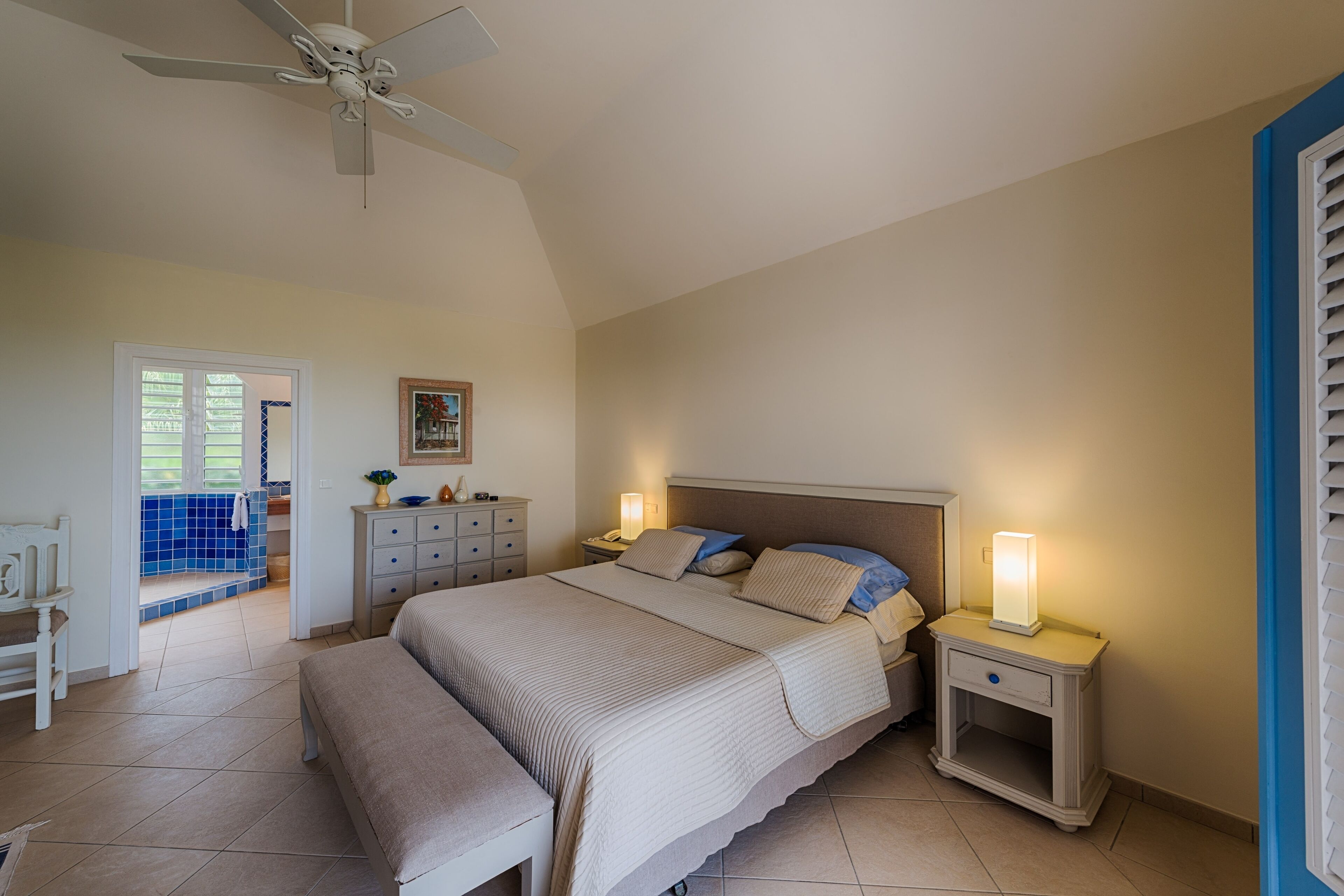 Une chambre dotée d’un grand lit, de tables de chevet, d’un ventilateur de plafond et offrant une vue sur l’extérieur.