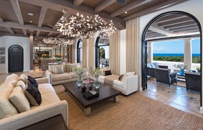 A spacious living area with a modern chandelier, comfortable seating, and a view of the ocean. - Elsewhere (8/10 Rooms) (Holetown)