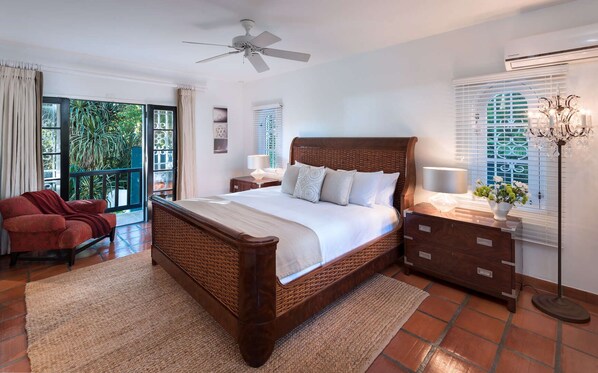 A bedroom with a large bed, a chair, a nightstand, a lamp, and a window with blinds.