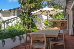An outdoor patio with a wooden table and chairs, an umbrella, and lush greenery. - Landmark (4/6 Rooms) Luxury house (Holetown)