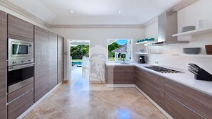 Une cuisine moderne dotée d’appareils électroménagers intégrés, d’un îlot central et offrant une vue sur une piscine et un jardin.