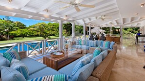 A covered outdoor seating area with a pool view, wicker furniture, and ceiling fans. - Moon Dance Luxury villa (Sandy Lane)