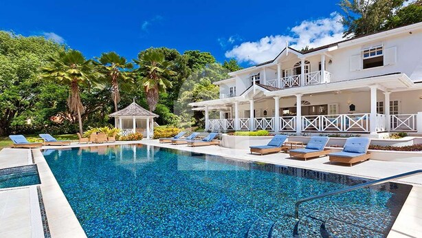 A large swimming pool with lounge chairs and a gazebo, surrounded by lush greenery and a white building with a balcony. - Moon Dance Luxury villa (Sandy Lane)