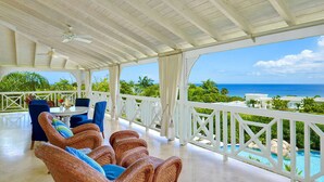 A covered outdoor seating area with wicker furniture and a view of the ocean.