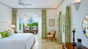 A bedroom with a bed, a chair, a table, and a dining area with chairs and a chandelier.