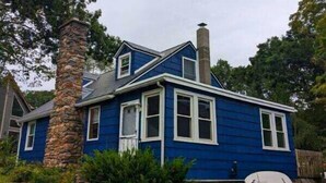 A two-story house with a stone chimney, blue siding, and a stone foundation. - Lakefront - King - W&D - PetsOK - Kayaks - SUPs (Coventry)