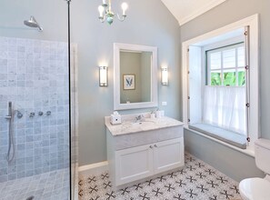 Un baño con ducha a ras de suelo, tocador con espejo y ventana con vistas a zonas verdes.