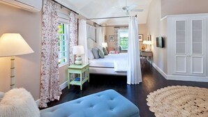 Een slaapkamer met een bed, een blauwe bank, een klein tafeltje met een lamp en een plafondventilator.