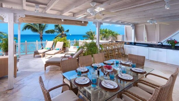 A covered outdoor dining area with a view of the ocean, furnished with wicker chairs and a glass table set for dining. - Reeds House Penthouse 14 (2/3 Rooms) (Lower Carlton)
