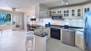 A modern kitchen with white cabinetry, a microwave, and a dishwasher. There is a bar area with stools and a view of the ocean. - Reeds House Penthouse 14 (2/3 Rooms) (Lower Carlton)