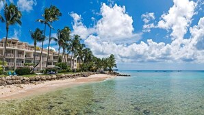 Een strandhotel met meerdere balkons, helder turquoise water en palmbomen.
