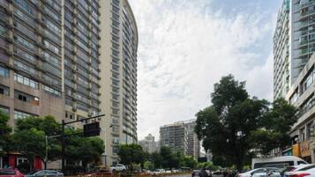 Vista de la calle con edificios residenciales altos, coches aparcados y un cielo despejado.