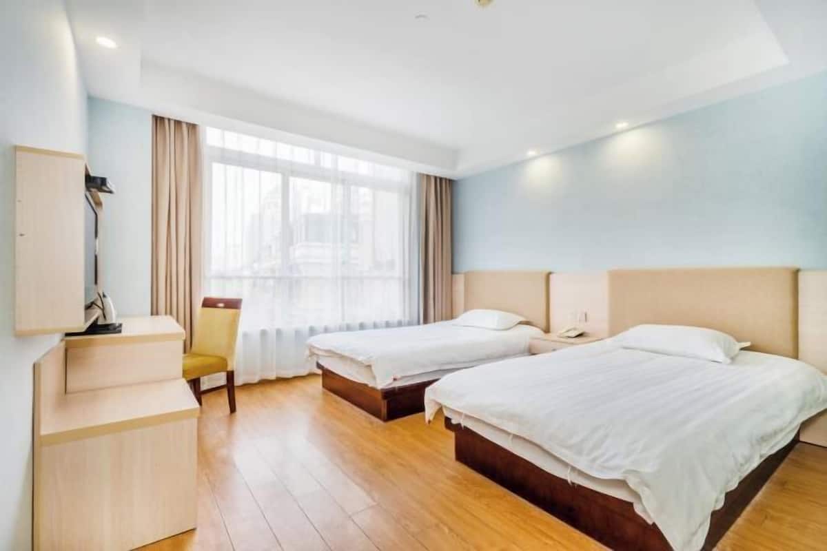 A hotel room with two beds, a desk, a chair, and a large window with curtains.